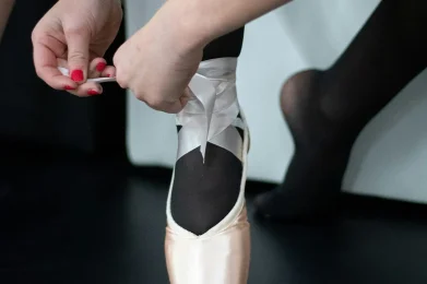 Ballet dancer tying pointe shoe ribbons before dance class at a Utah ballet studio.